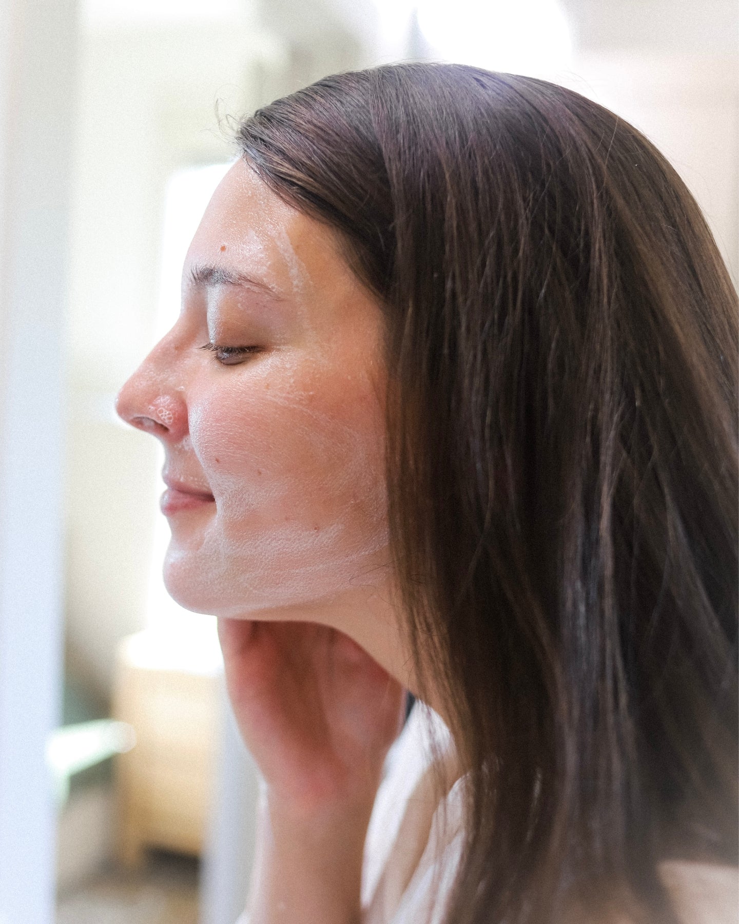 A close-up profile shot of a woman with the Clarifying Cleanser lathered on her face.