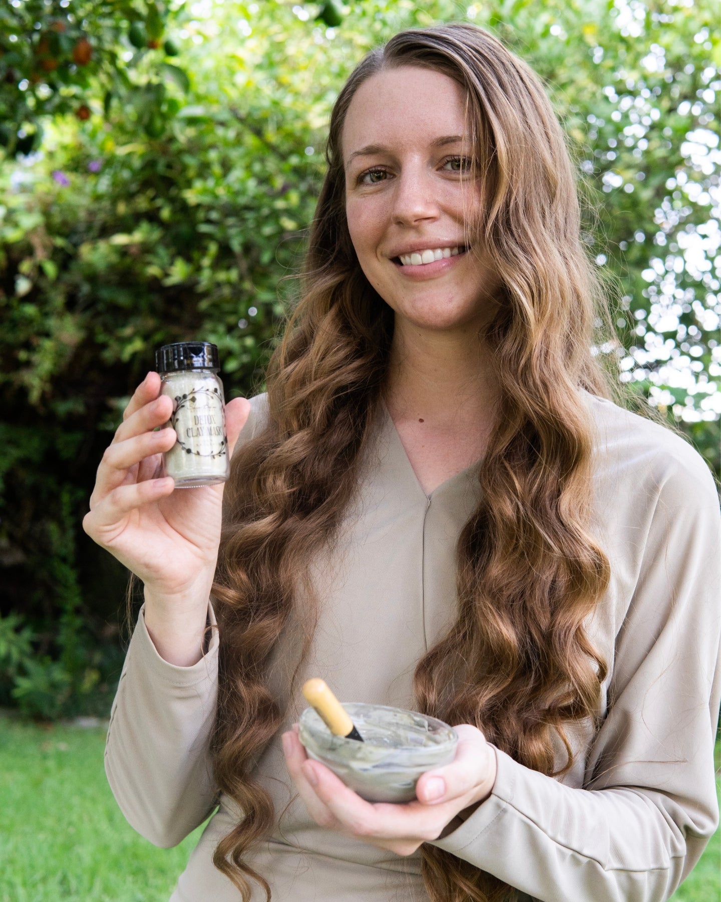 A smiling woman holds a jar of the Detox Clay Mask.