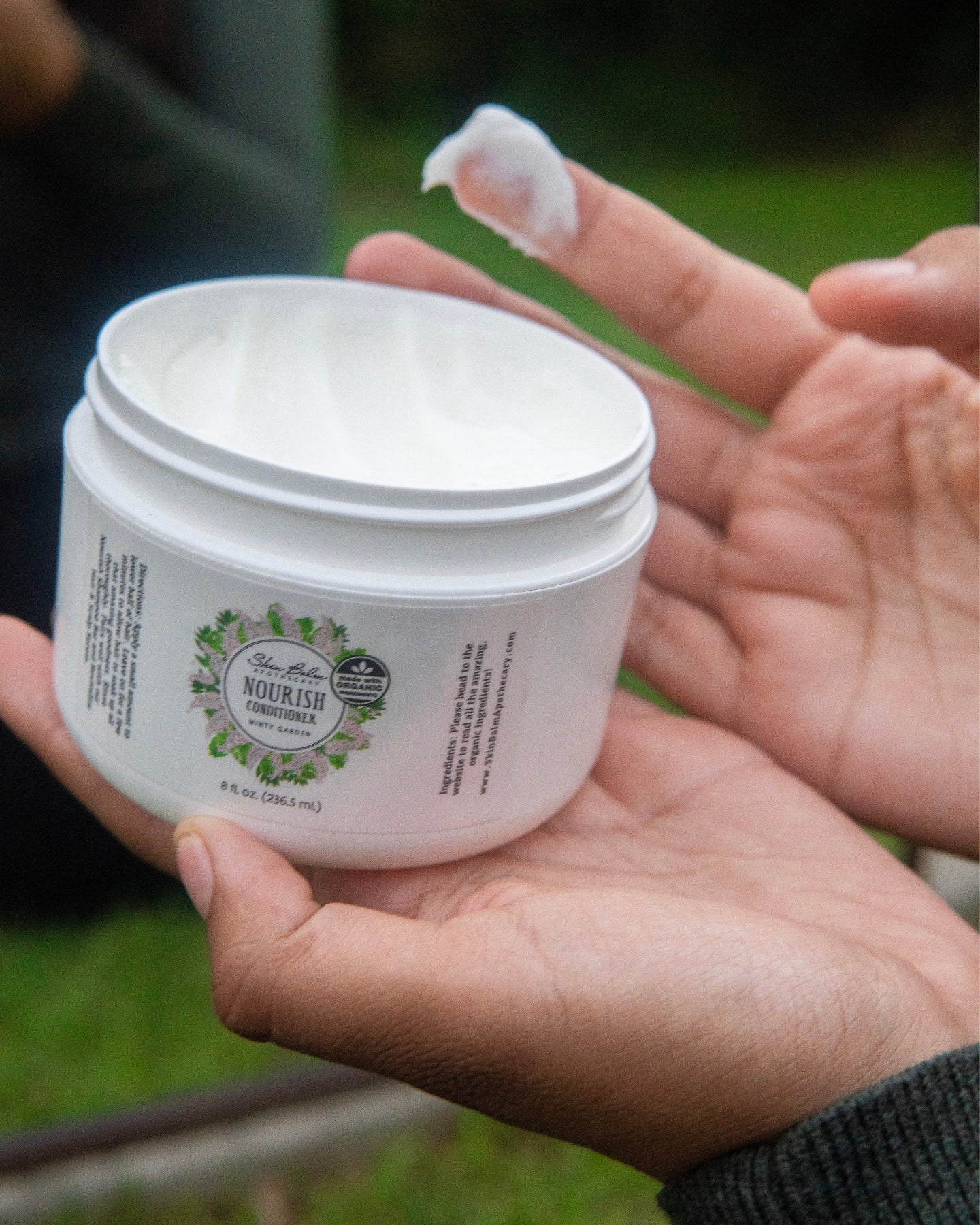  A close-up shot of a woman scooping Minty Garden Nourish Conditioner out of the container.