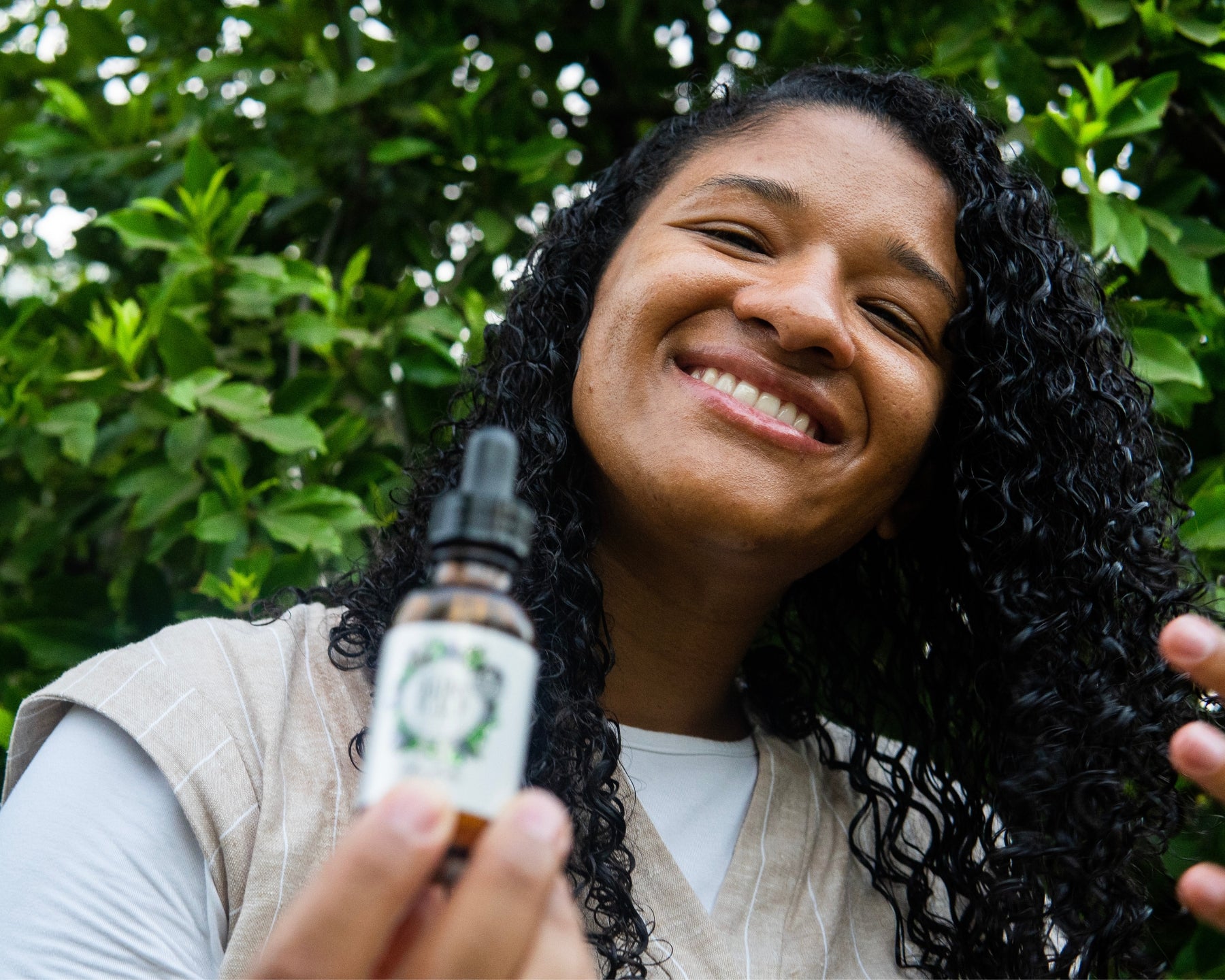 Revitalize Hair & Scalp Serum blurred in the foreground with a smiling woman twirling her hair focused in the background.