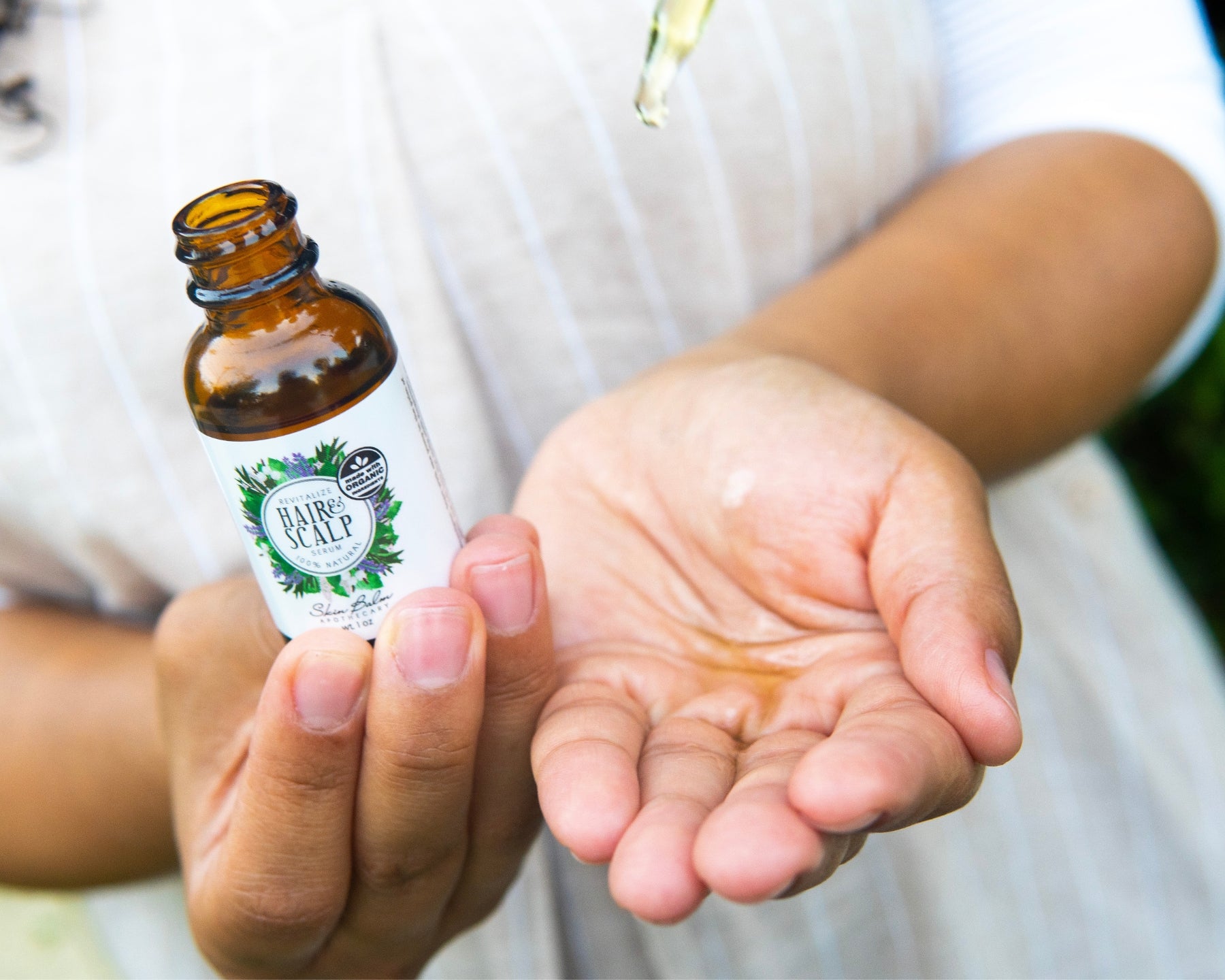 A close-up shot of the Revitalize Hair & Scalp Serum being dispensed into an open palm from the dropper.