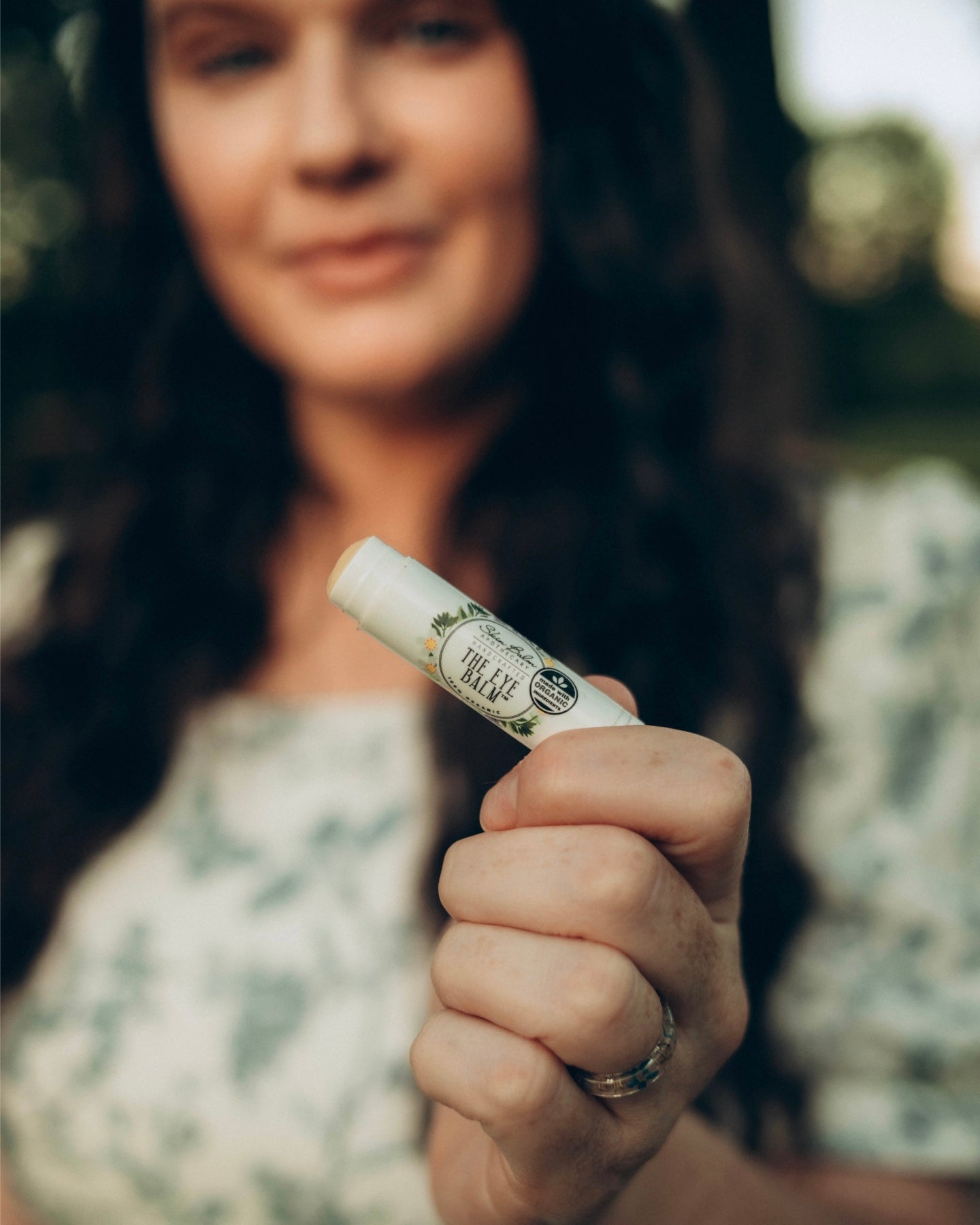 A close-up shot of The Eye Balm™ with the woman holding the product blurred in the background.